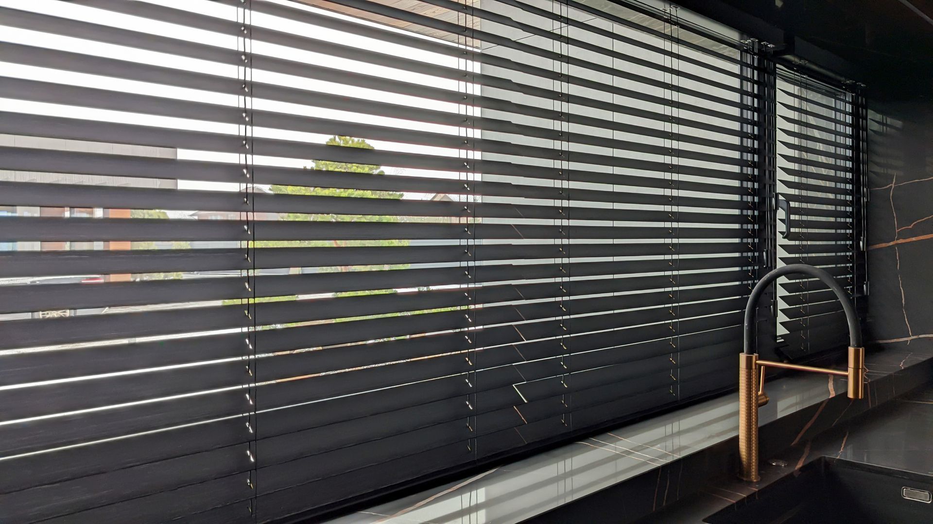 Sleek black faux wood kitchen window blinds above a sink with a copper and black faucet