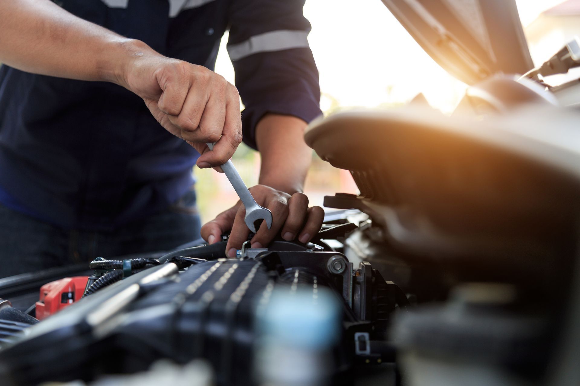 A man is working on the engine of a car with a wrench.