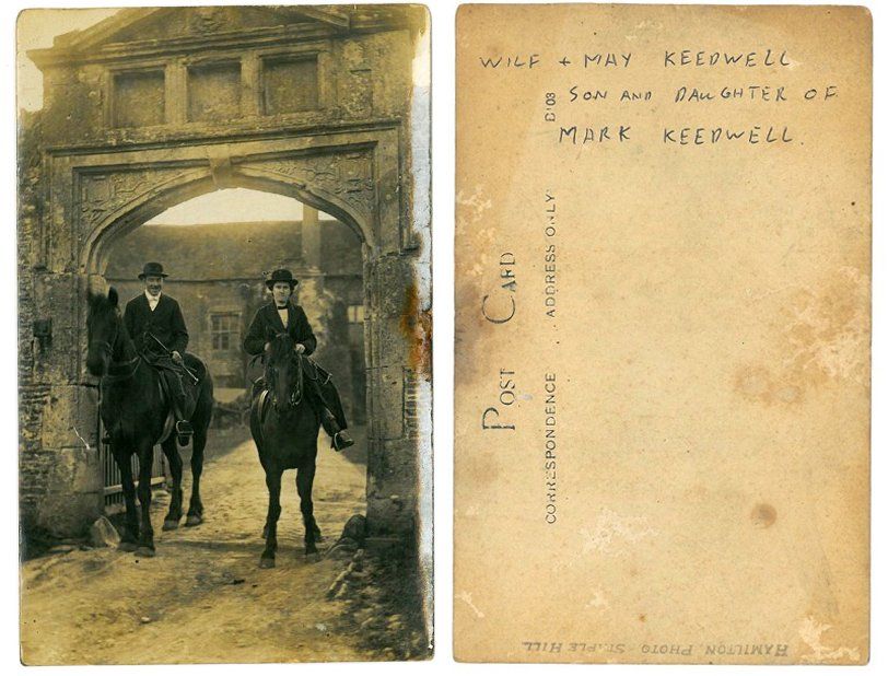 Two men are riding horses in front of a stone archway