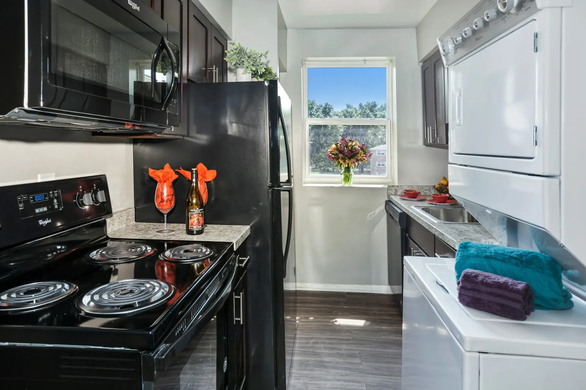 Galley-style apartment kitchen with black appliances, a window, and a stacked washer/dryer.