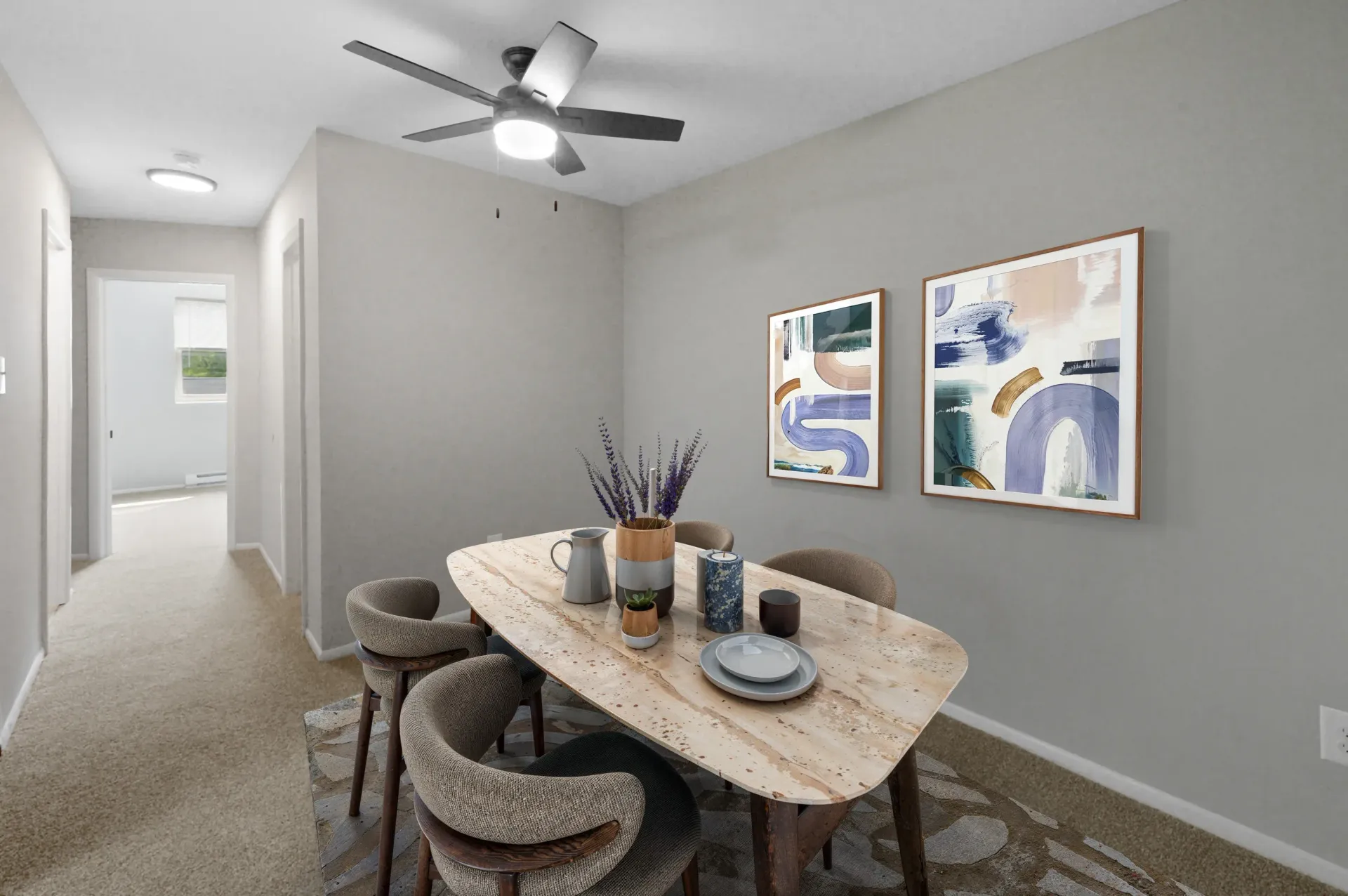 Dining area in a modern apartment with a wooden table, chairs, wall art, and a ceiling fan.