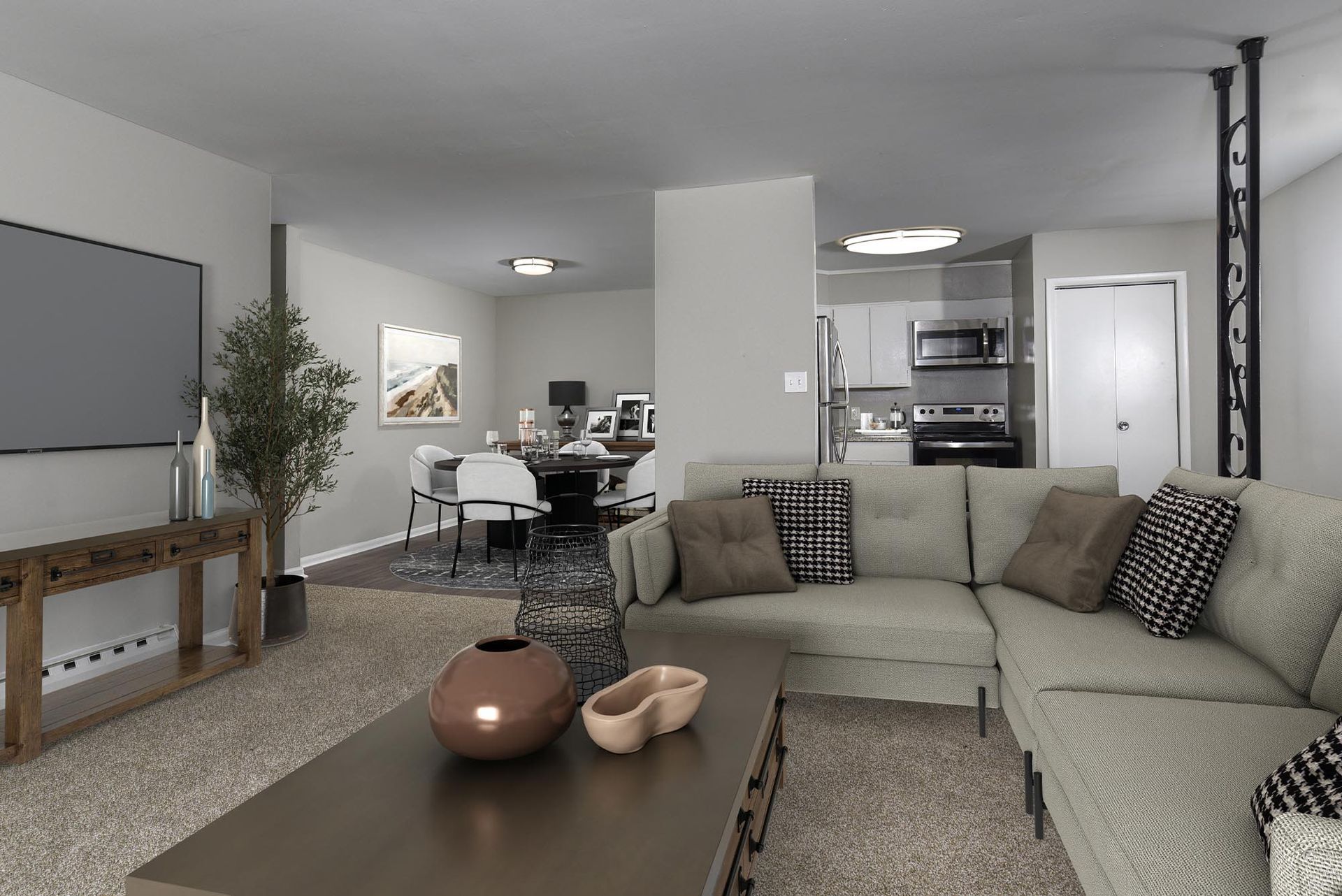 Open-concept living room with a light-gray sectional sofa, coffee table, and kitchen visible in the background.