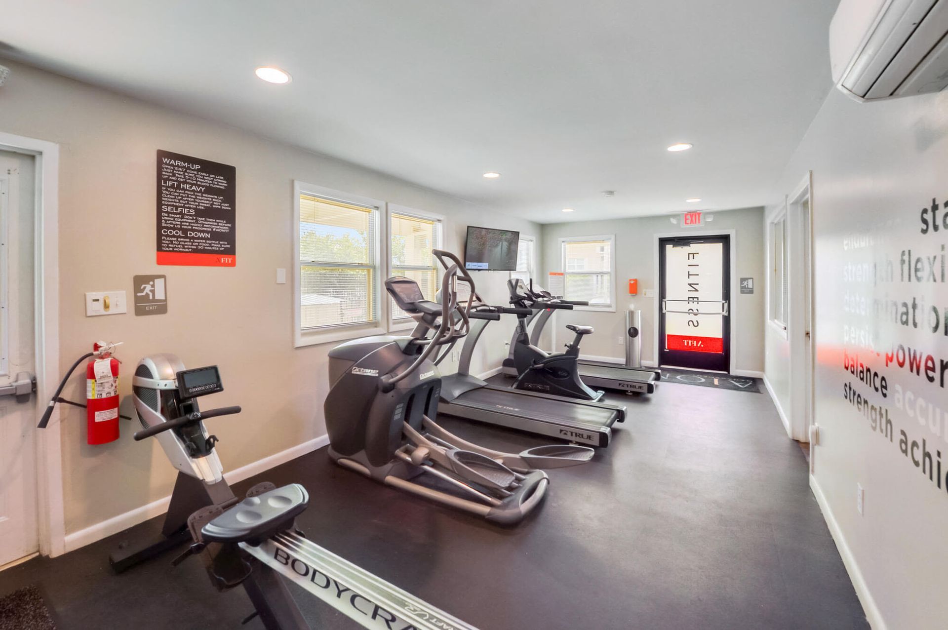 Indoor apartment gym with treadmills, an elliptical, a stationary bike, and a wall-mounted TV.