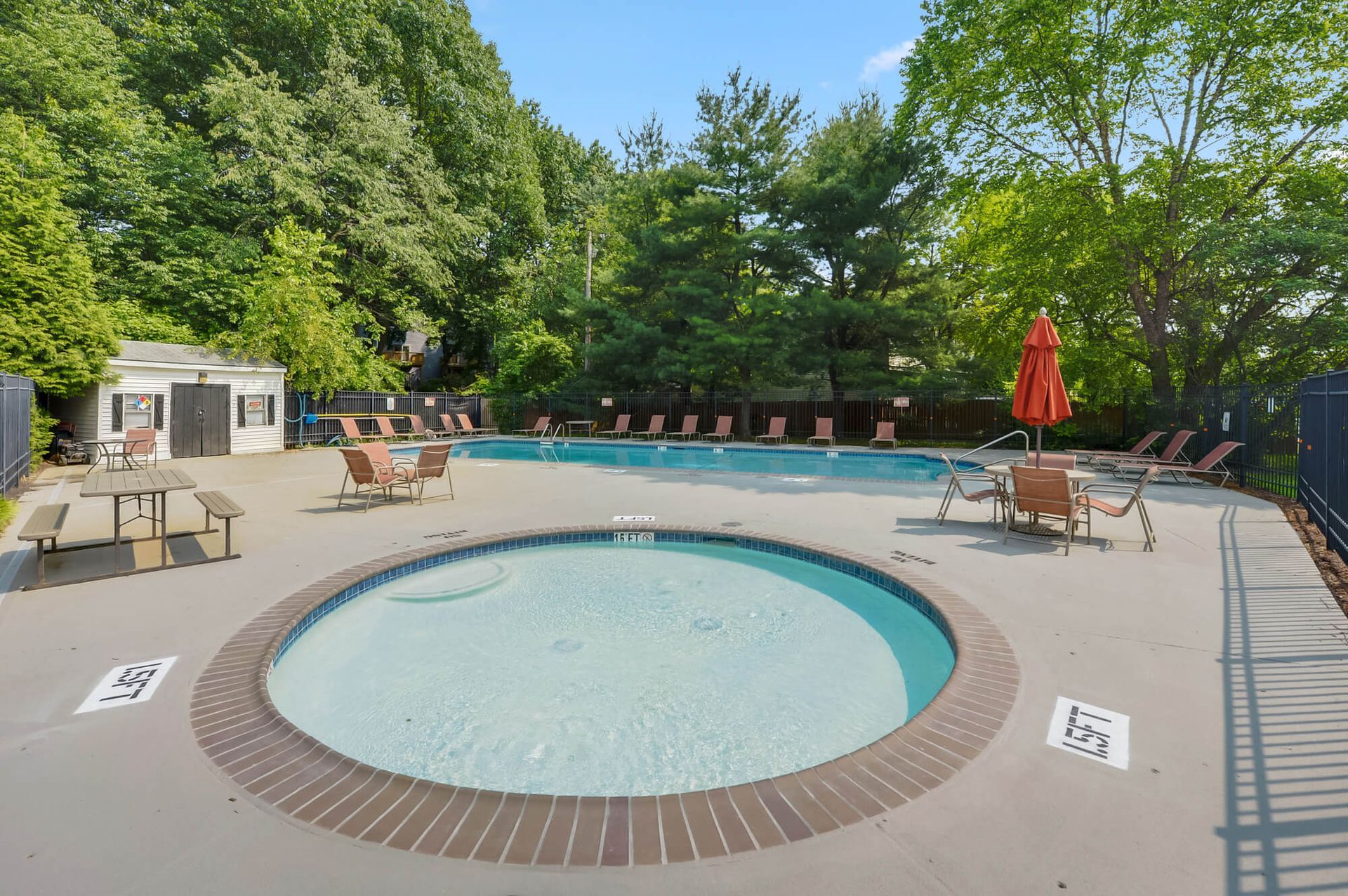 Outdoor community pool with a circular hot tub in the foreground and surrounding lounge chairs.