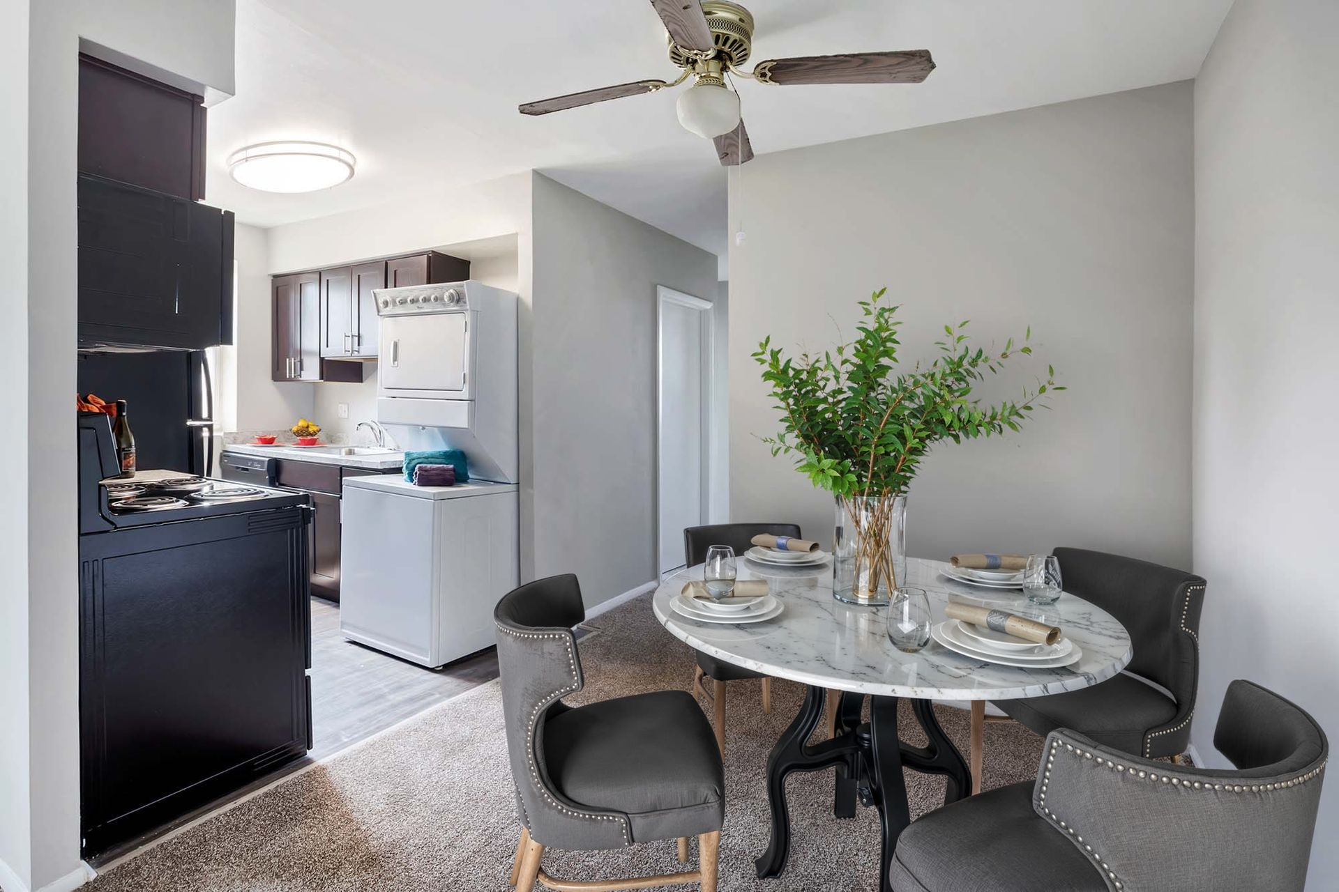 Dining area with a round marble table, gray upholstered chairs, and a compact kitchen in the background.