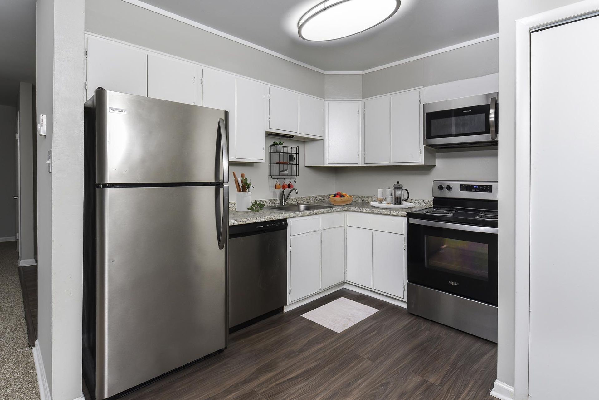 Kitchen in an apartment with stainless steel refrigerator, dishwasher, microwave, stove, and white cabinets.