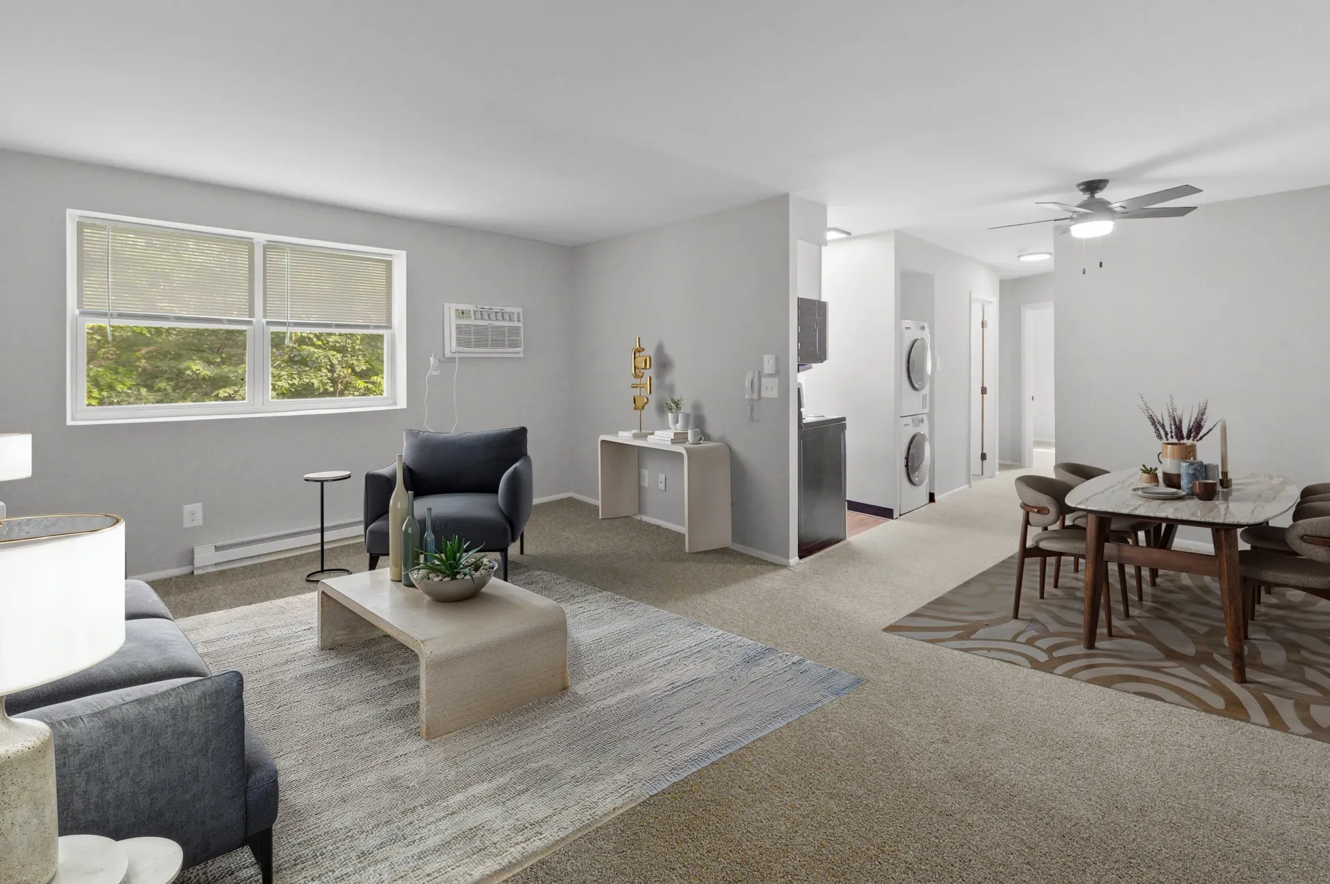 Bright living room with two windows and seating; hallway shows a stacked washer/dryer.