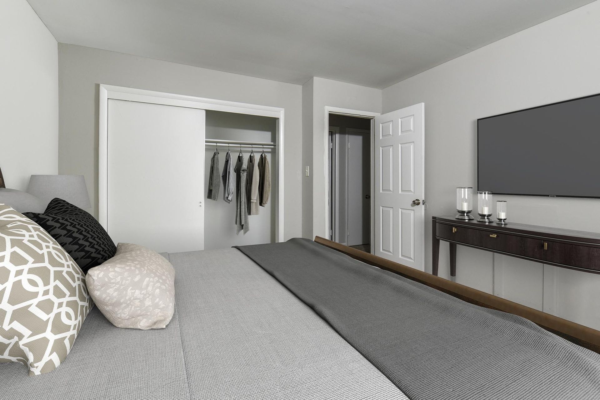 Bedroom interior with a bed, open closet, dresser, and a wall-mounted TV.
