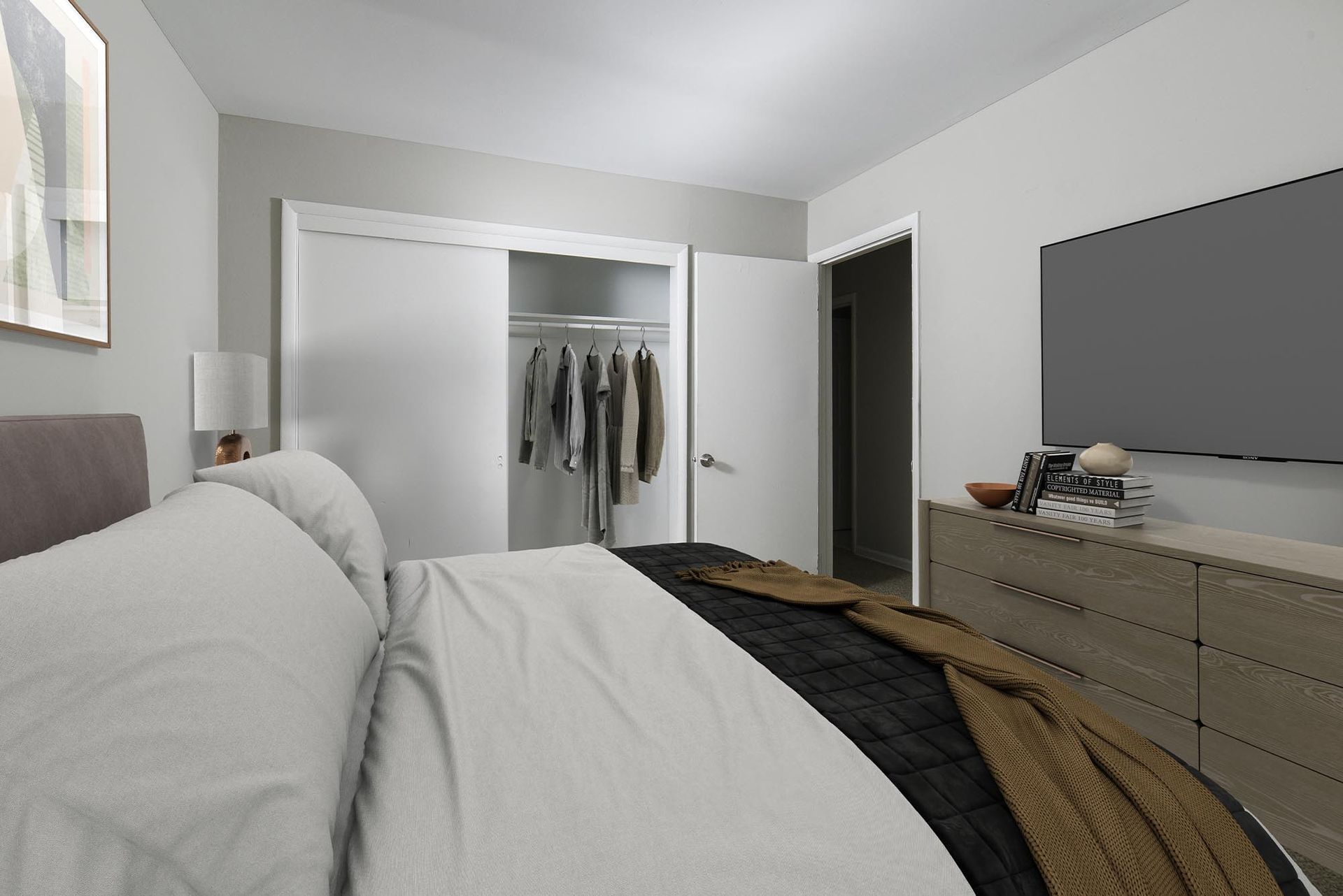 Bedroom in an apartment with a bed, dresser, TV, and open closet.