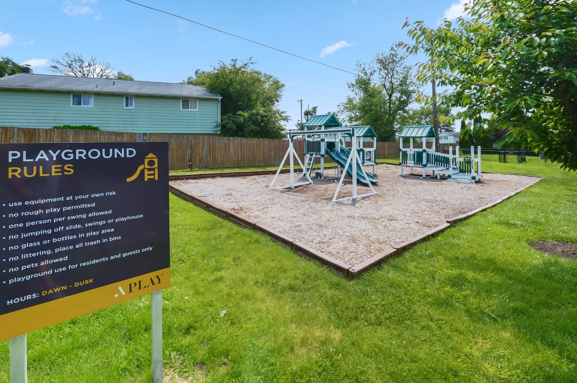 Playground with slides on a wood-chip surface and a rules sign in the foreground.