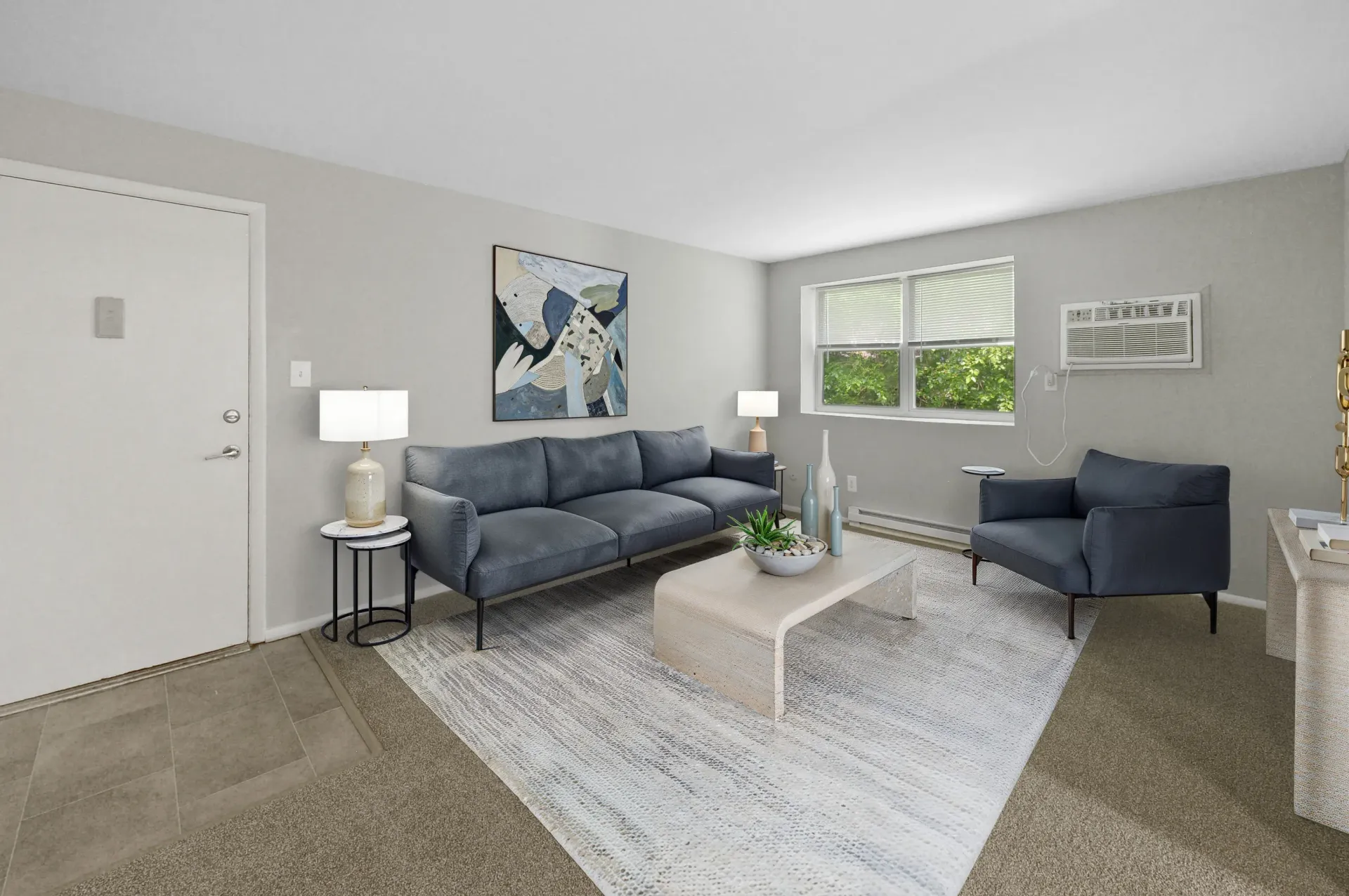 Living room in a modern apartment with gray walls, blue sofa, chair, coffee table, and art.