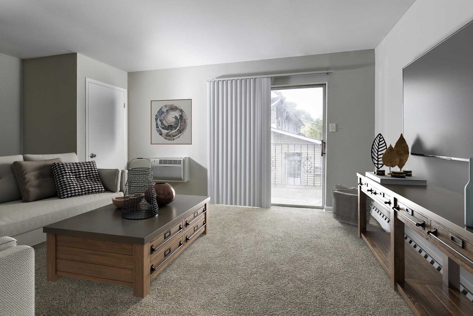 Living room in an apartment with neutral decor, beige carpet, a sofa, coffee table, and sliding door to balcony.