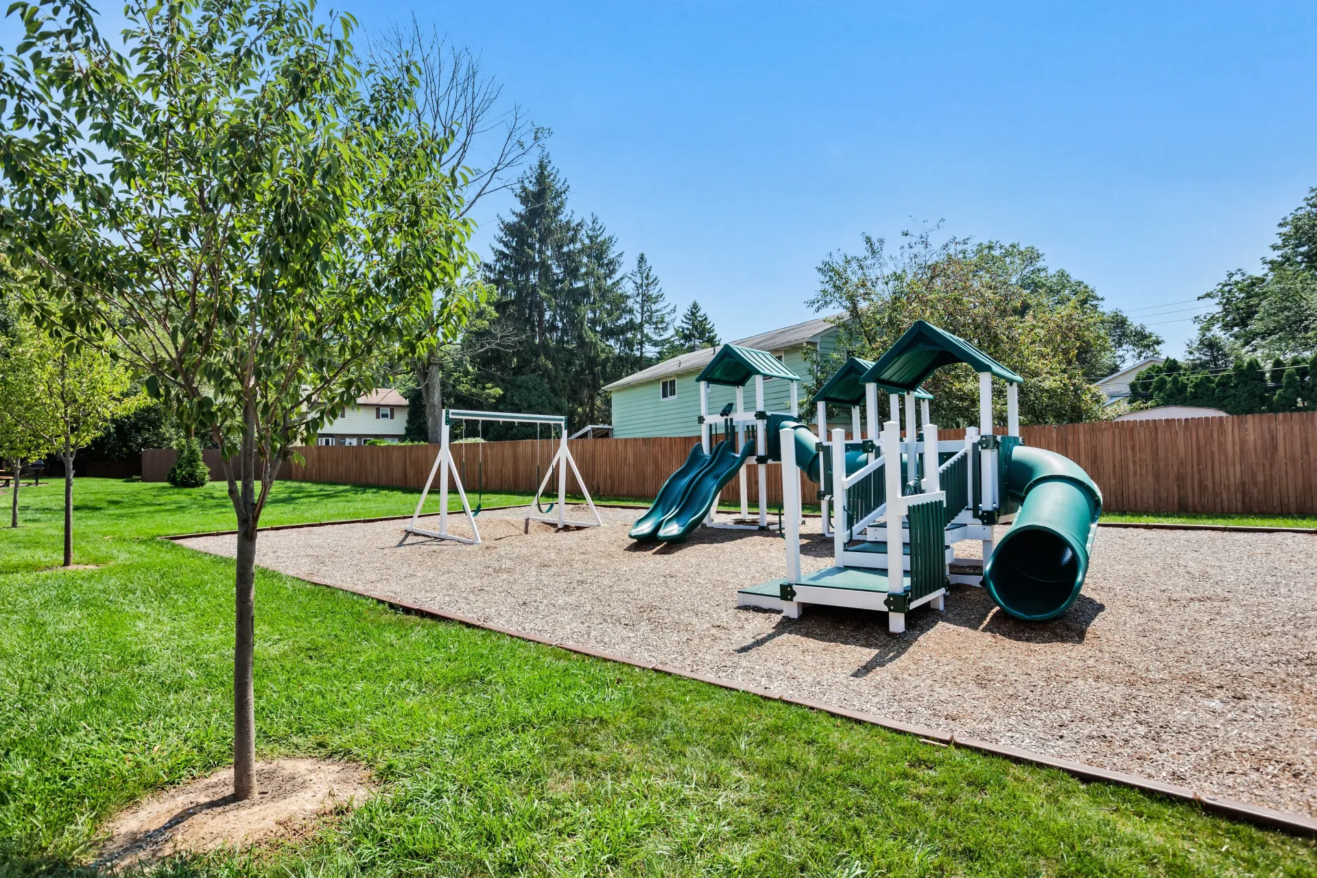 Playground with slides and swings in a fenced, grassy community area.