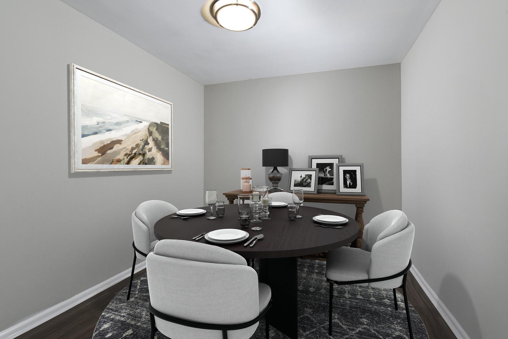 Dining area with a round dark table and light gray chairs in a neutral-toned apartment.