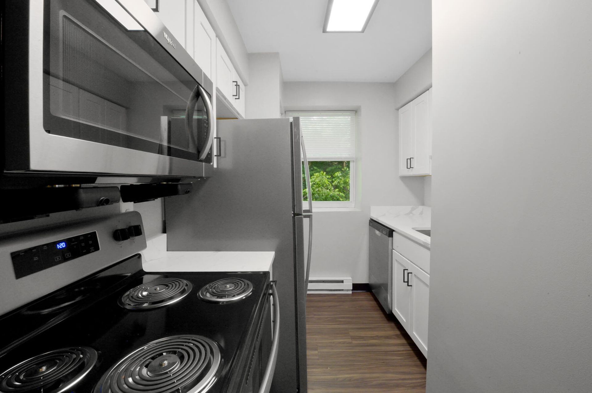 Compact galley kitchen with stainless steel appliances, white cabinets, and a window.