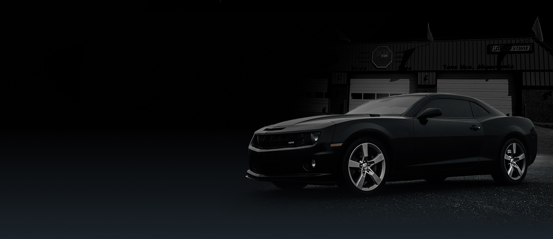 A black car is parked in front of a garage in the dark. | Brakes For Less