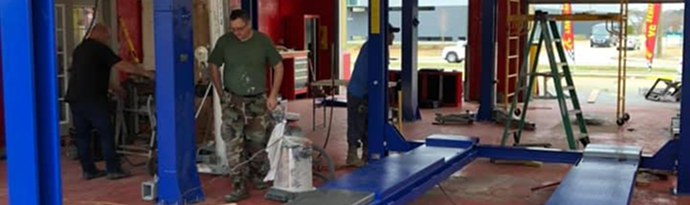 A man is standing in a garage with a vacuum cleaner. | Brakes For Less