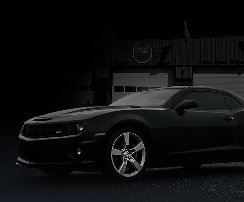 A black car is parked in front of a garage door. | Brakes For Less