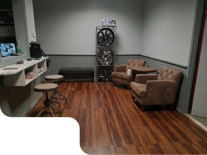 A waiting room with chairs , tables and a stack of tires on the wall. | Brakes For Less