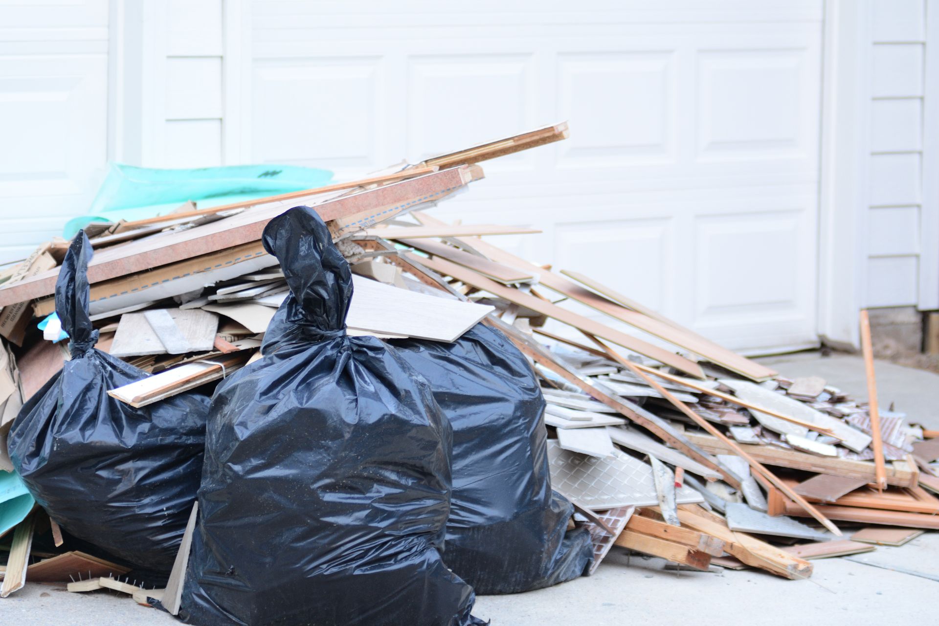 Black trash bags and wood debris in front of a white garage door.