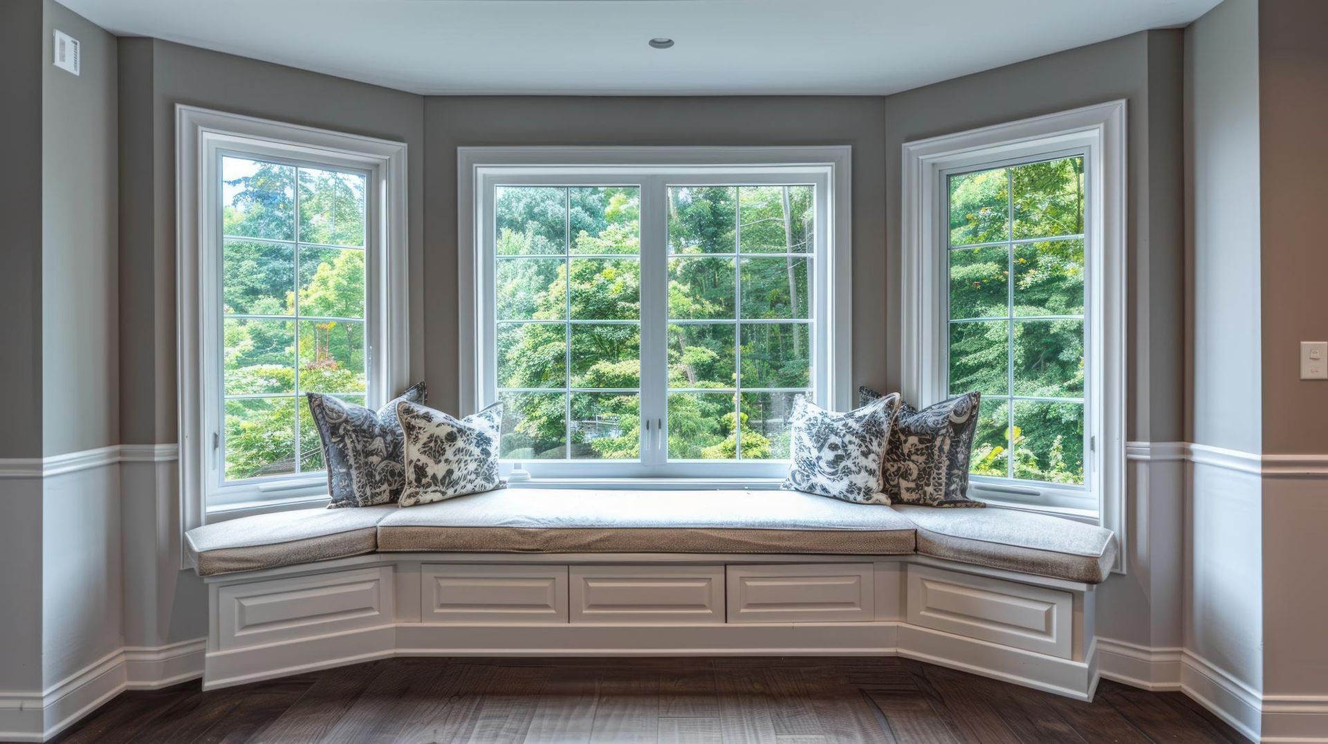 Built-in bay window seat with cushions and pillows in a bright room overlooking trees