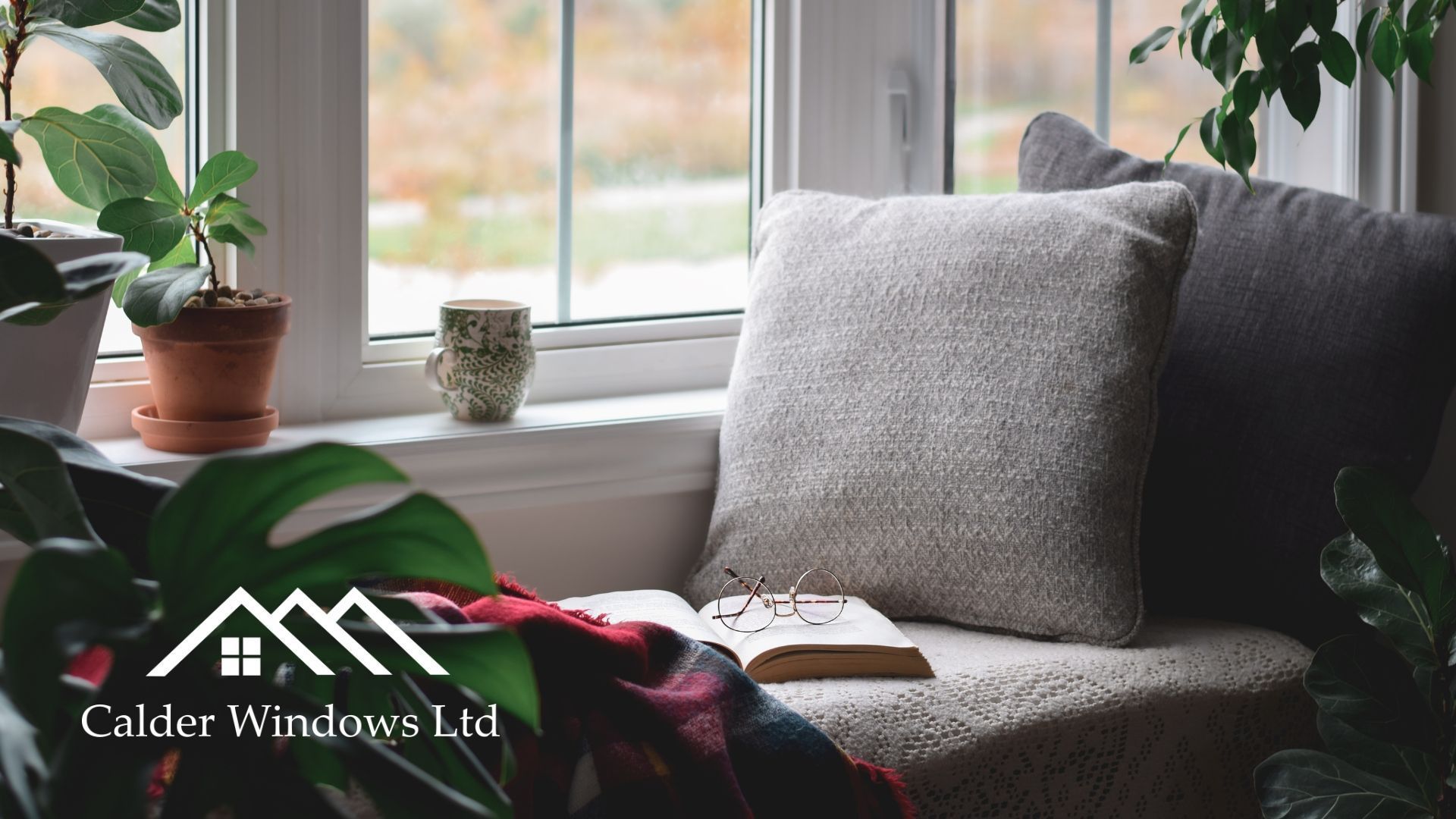 Cozy window seat with gray cushions, potted plants, and an open book in soft natural light