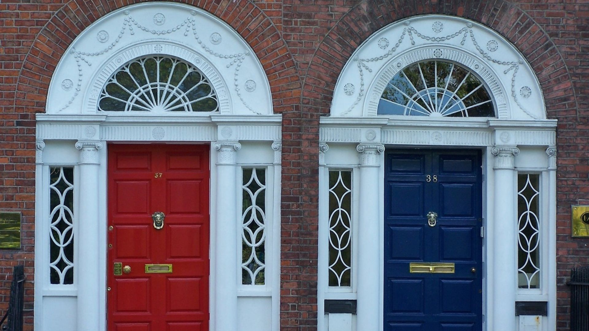 Two ornate front doors on a brick building, one red and one dark blue, with arched white trim.
