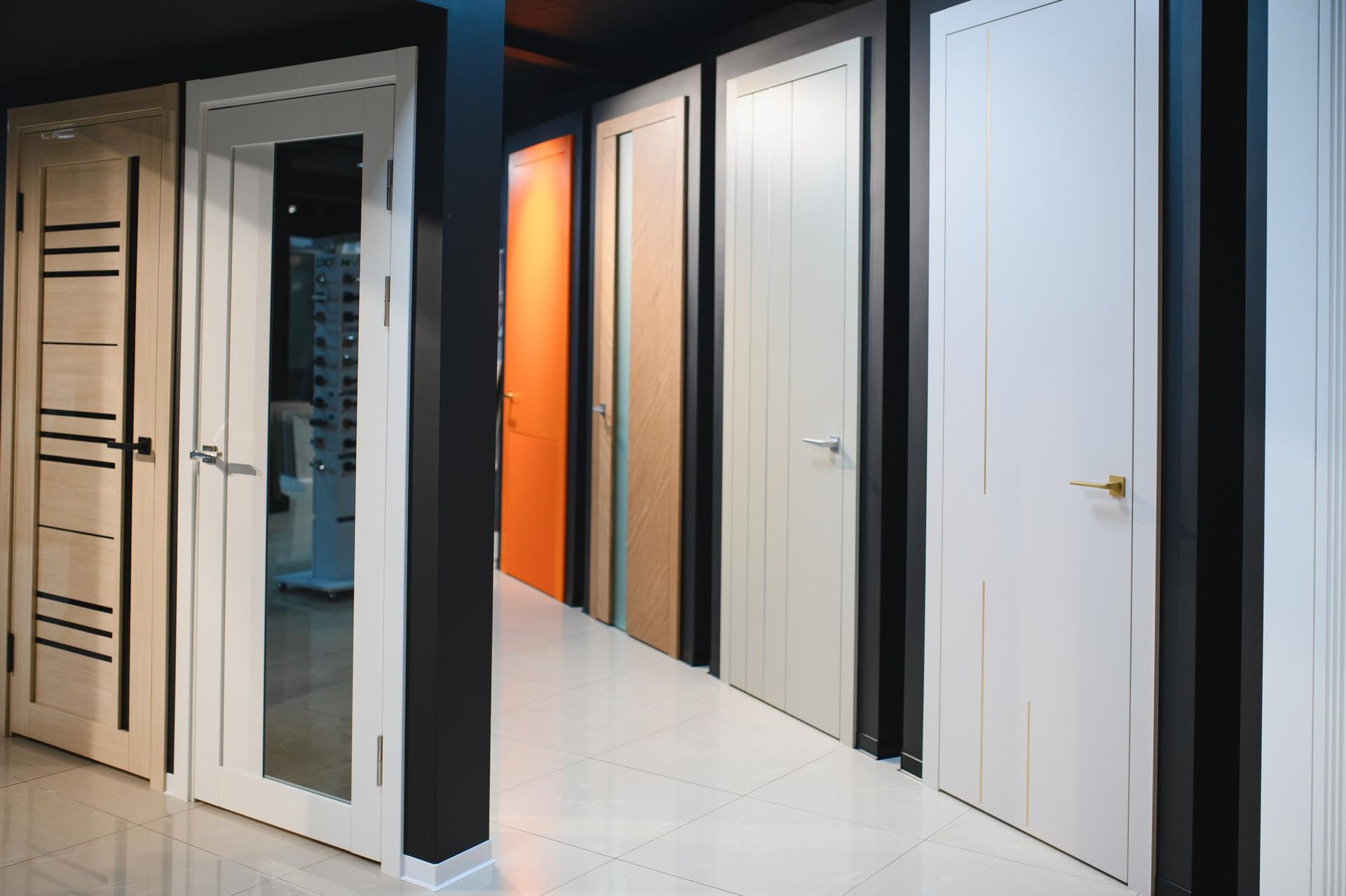 Showroom display of modern interior doors in white, black, beige, and orange along a hallway