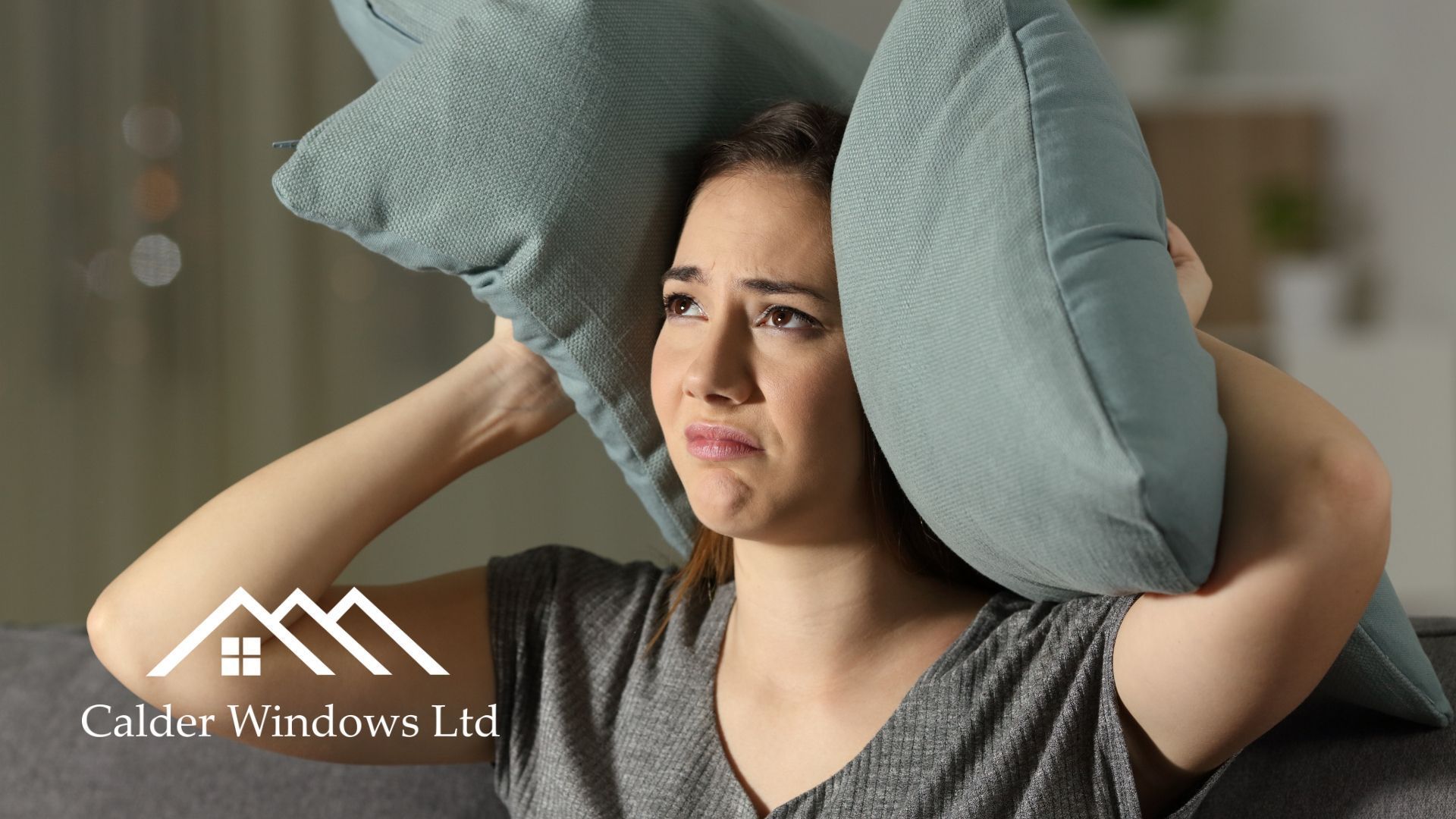 Woman holding pillow over ears, looking frustrated in a home interior.