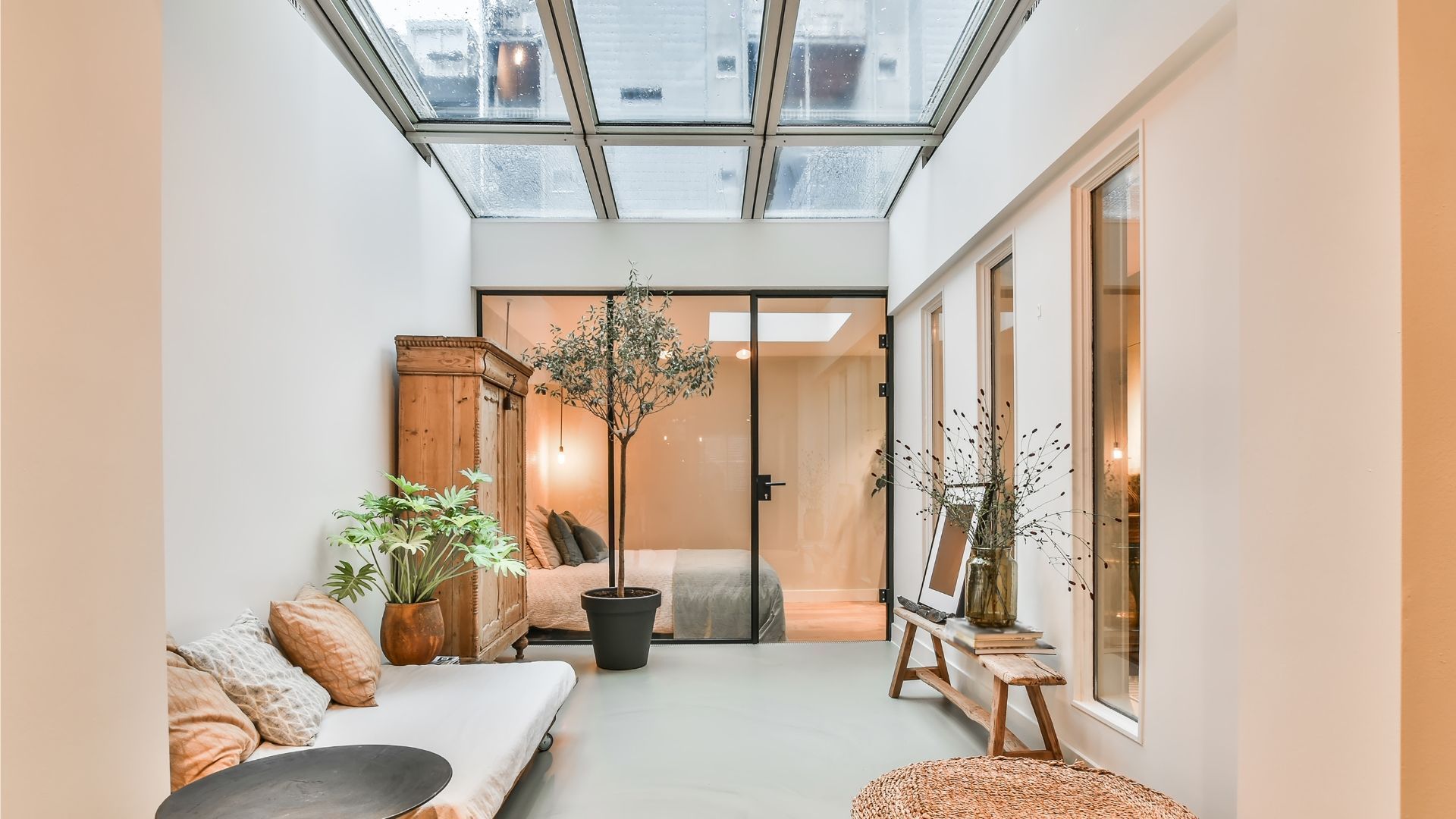 Bright indoor courtyard with potted plants, wicker seating, and glass doors under a skylight.