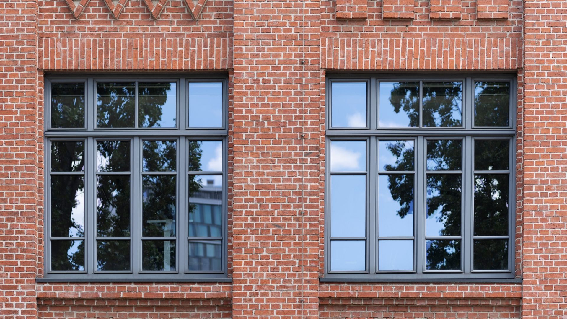 Brick building facade with two large black-framed windows and reflections of trees outside