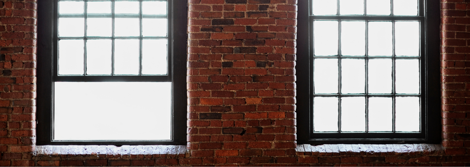Two white-framed windows set in a red brick wall, with one open pane on the left.