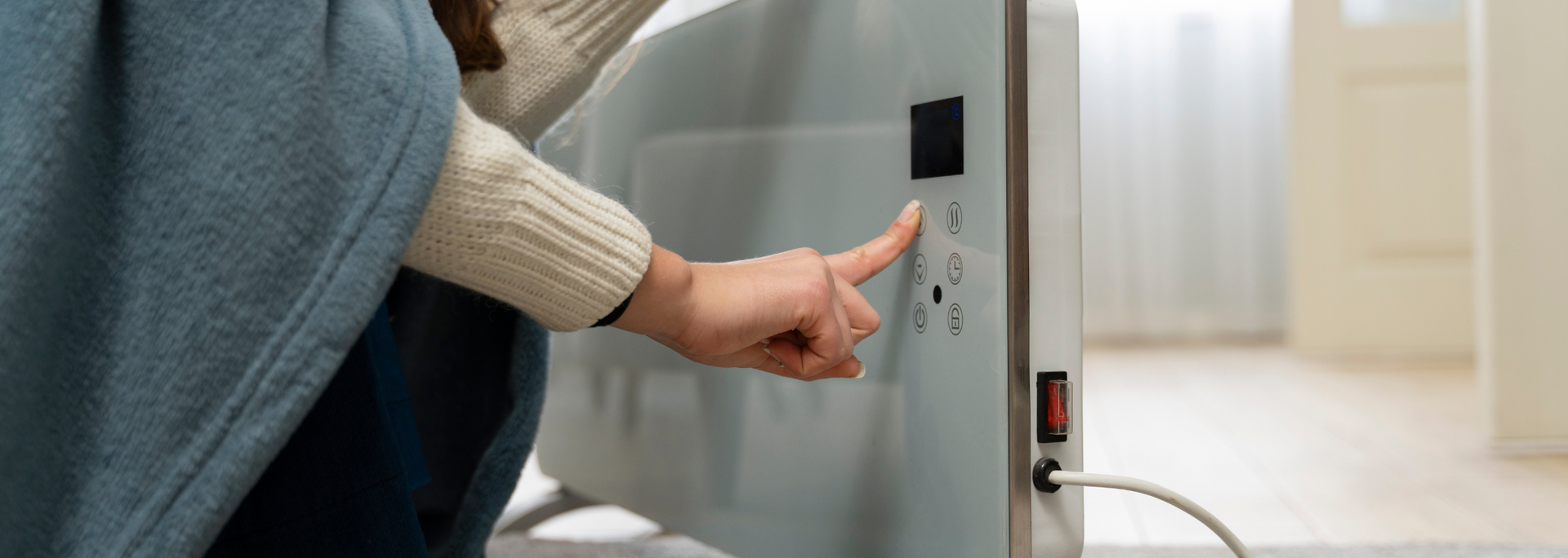 Person presses a button on a white electric heater beside a sunlit window