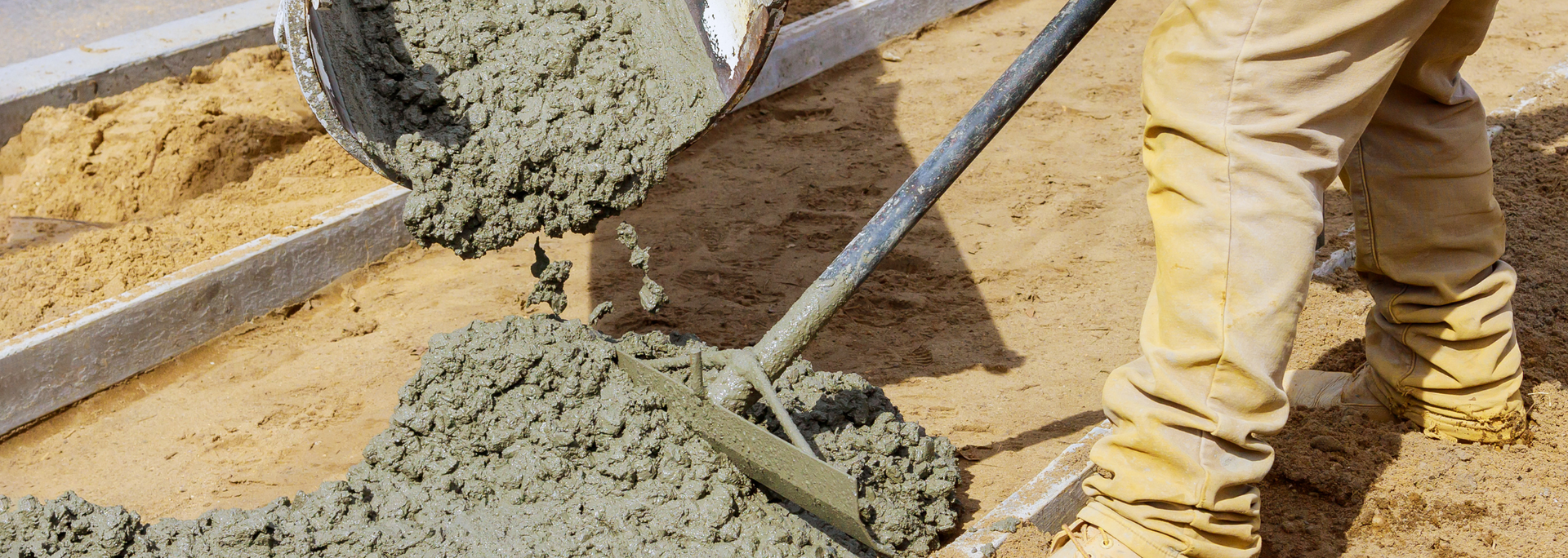 Workers pouring wet concrete into a construction form with shovels and a wheelbarrow
