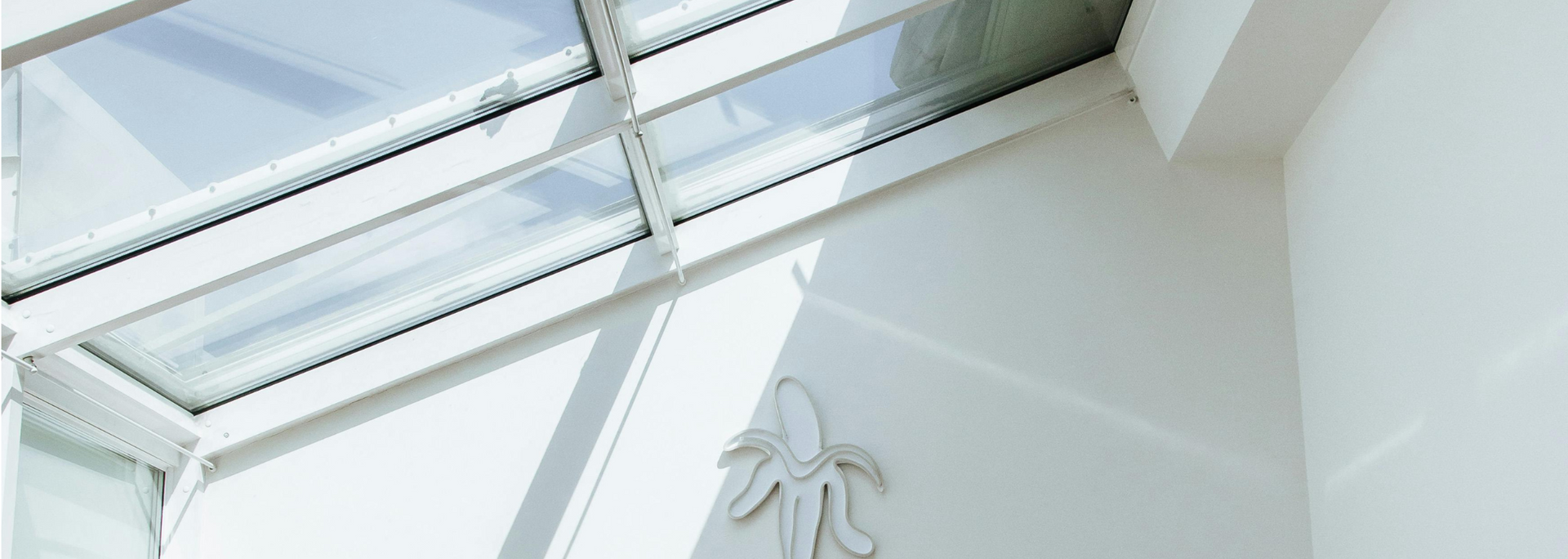 Skylight ceiling with sunlight casting angular shadows on a white wall.