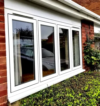 White-framed bay windows on a brick house with shrubs below