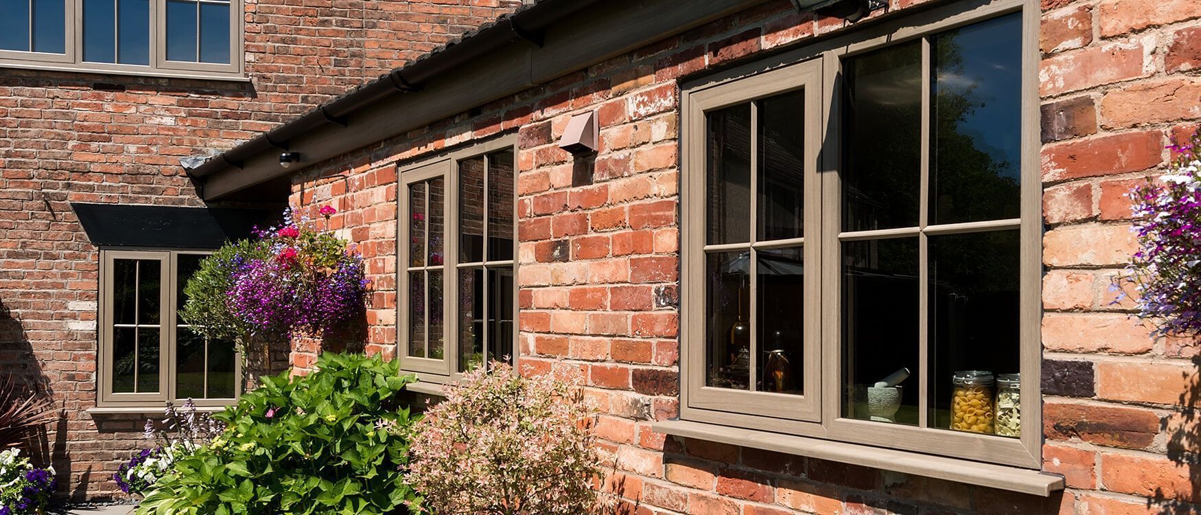 Brick house exterior with beige-framed windows and a flowering hanging basket in sunlight
