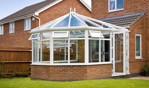 Brick house with a white-framed glass conservatory and a clear roof, set in a grassy backyard.
