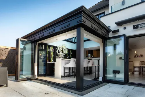 Modern glass sunroom with open doors, black trim, and a kitchen-dining area inside