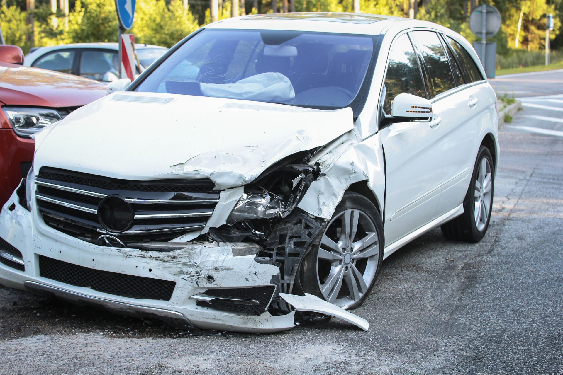 A white car with a damaged front end is parked next to a red car.