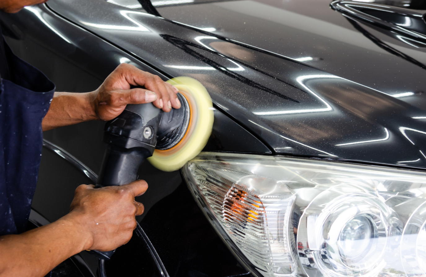 A man is polishing the hood of a car with a polisher.