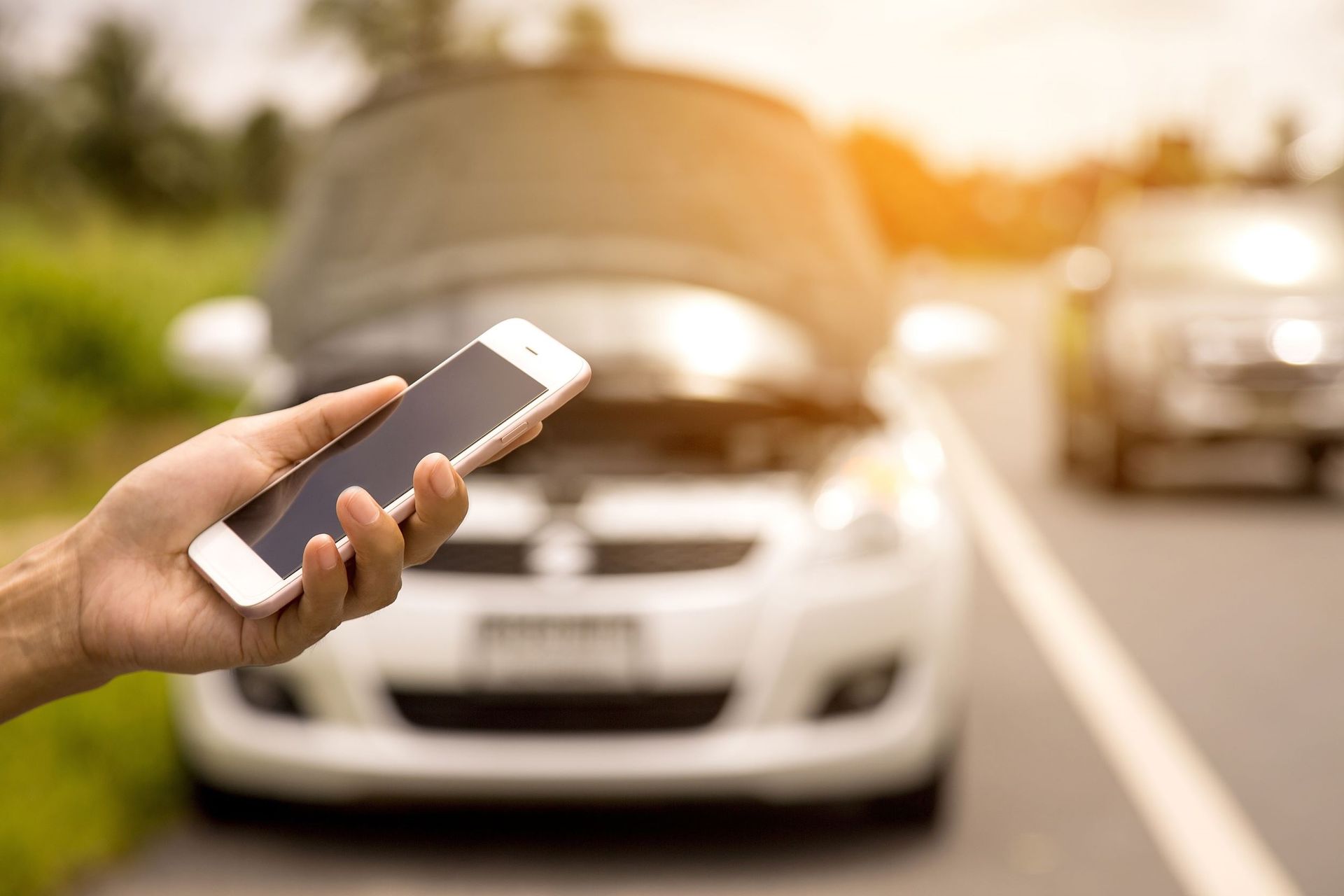 A person is holding a cell phone in front of a broken down car.