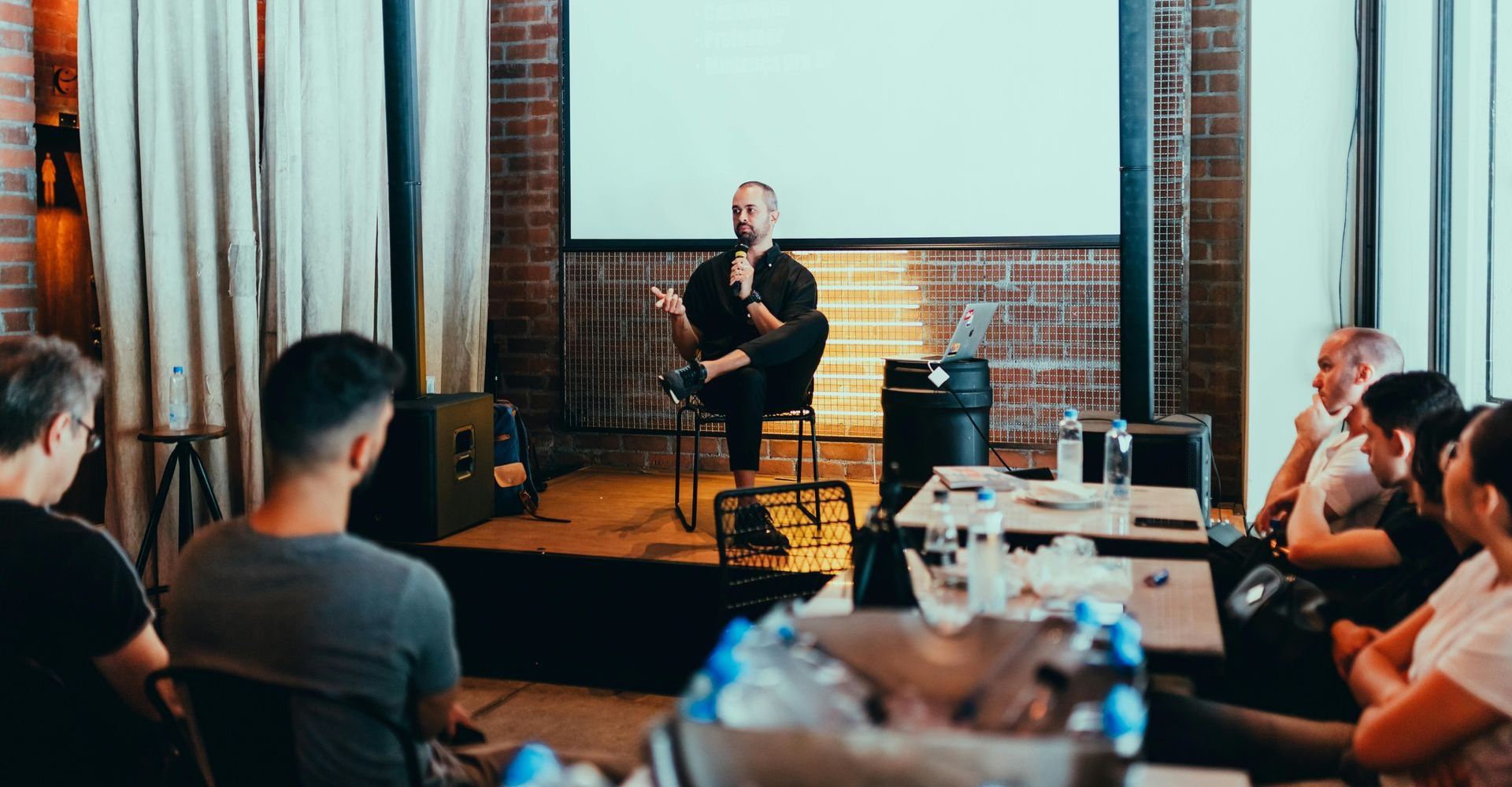 a man is sitting on a stage giving a presentation to a group of people.