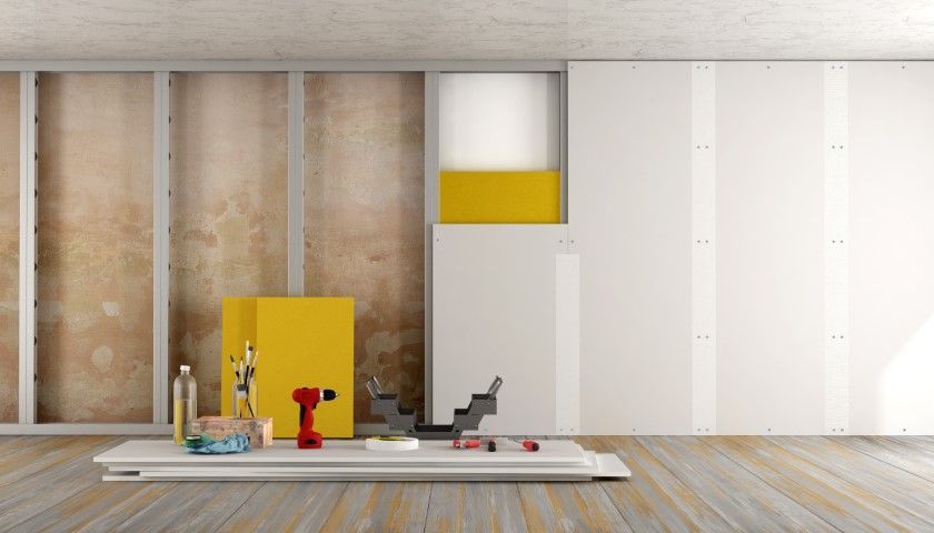 Interior construction with exposed studs, drywall, tools, and a yellow box.