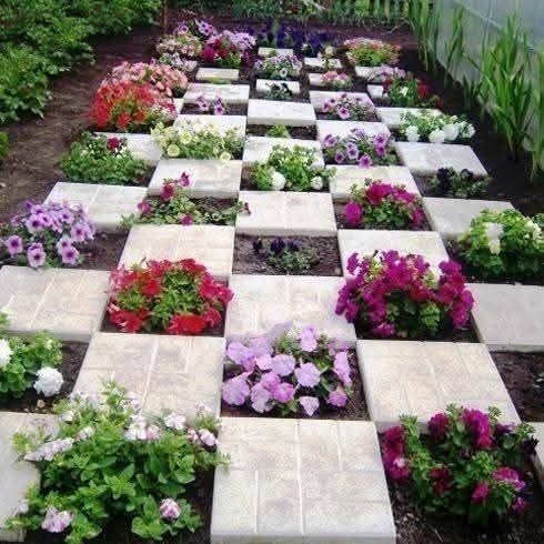 Un sentiero da giardino realizzato con lastre quadrate disposte a scacchiera, con fiori colorati piantati negli spazi alternati.