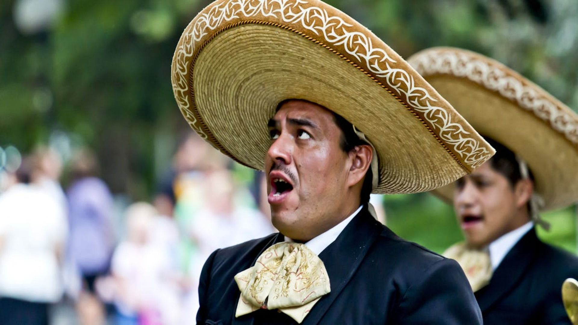 Un hombre que lleva un sombrero y una pajarita está parado frente a una multitud.