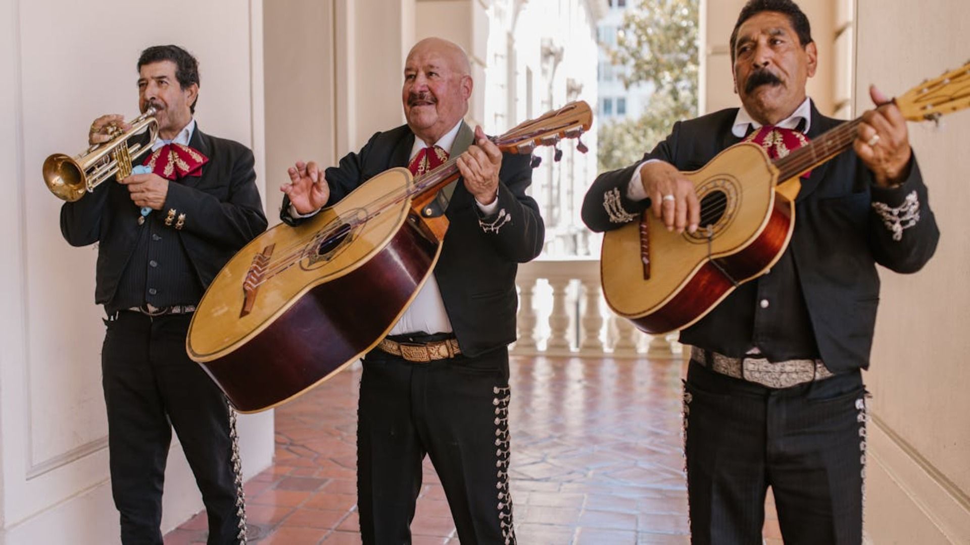Tres cantantes de mariachi tocan guitarras y una trompeta en un pasillo.
