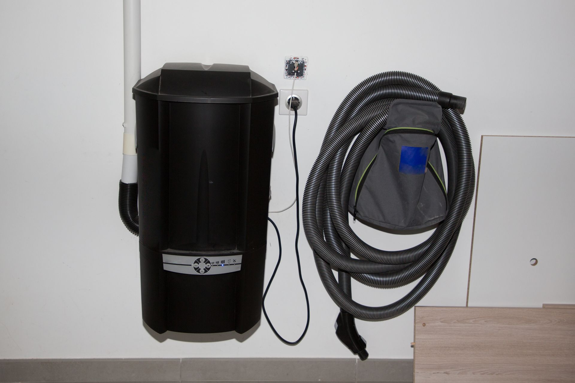 A Black Vacuum Cleaner Is Hanging on A Wall Next to A Hose