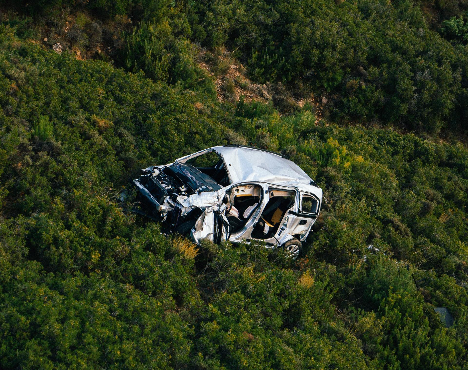 Una vista aérea de un automóvil que se estrelló contra una colina rodeada de árboles.
