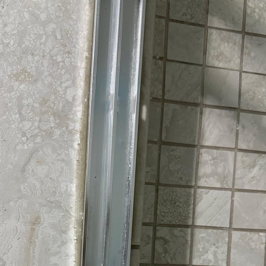 Close-up of a metal shower door frame beside beige tiled bathroom wall